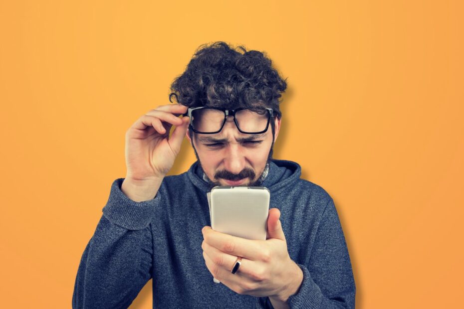 Homem tentando enxergar o celular com dificuldade, representando dúvidas sobre qual a melhor operadora de celular.